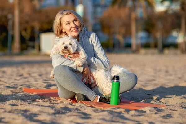 Elderly woman resting on the beach with a dog.