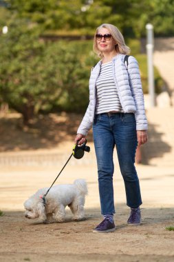 Çekici orta yaşlı sarışın kadın yaz şehrinde köpekle yürüyor.