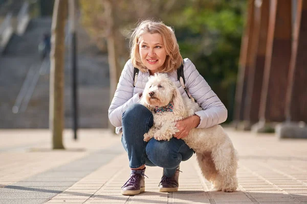 Mulher madura andando com cachorro branco fofo na cidade de verão — Fotografia de Stock