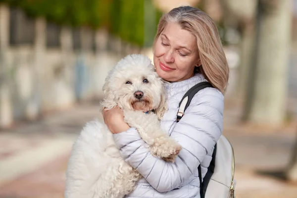 Mulher de meia-idade andando com cachorro branco fofo na cidade de verão — Fotografia de Stock