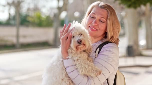 Женщина средних лет гуляет с пушистым белым псом в летнем городе — стоковое видео