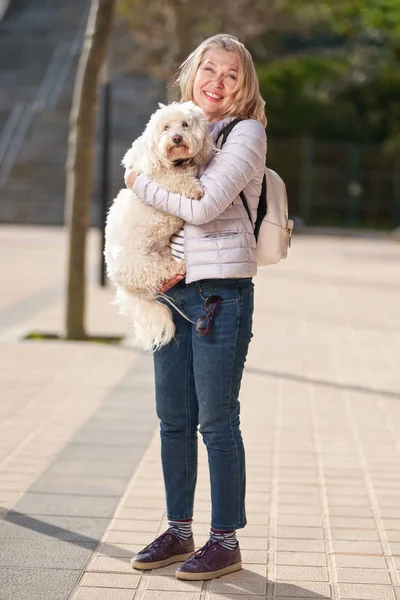 Mature woman walking with fluffy white dog in summer city — Stock Photo, Image