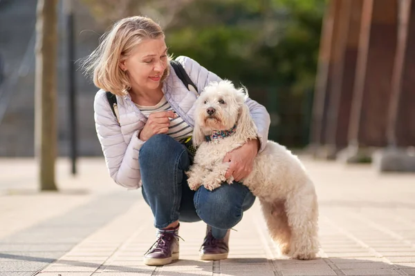 Gammal kvinna promenader med fluffig vit hund i sommar stad — Stockfoto