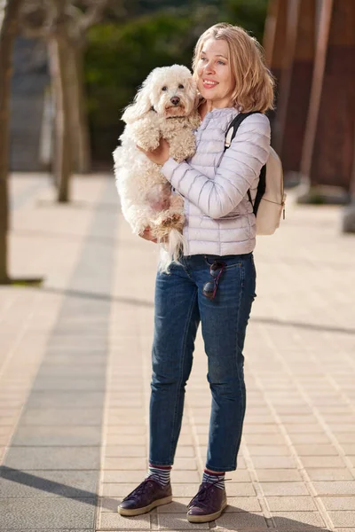 Mujer madura paseando con un perro blanco esponjoso en la ciudad de verano — Foto de Stock