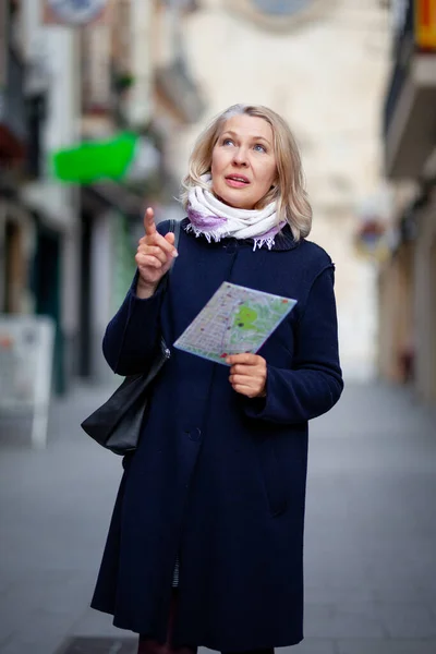 Elinde harita olan bir kadın turist şehrin sokaklarında yürüyor. — Stok fotoğraf