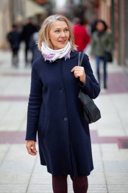 Mutlu emekli kadın bir turist şehrinin sokaklarında yürüyor.