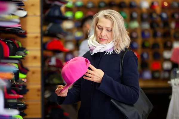 Women in hat store chooses baseball cap.