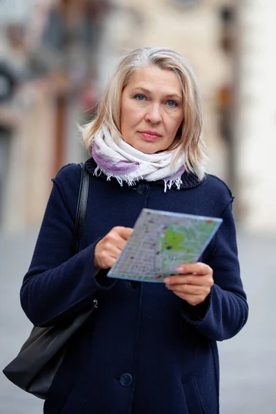 Turista mujer madura con un mapa en la mano pasea por las calles de la ciudad —  Fotos de Stock