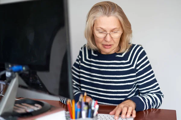 Γυναίκα μέσης ηλικίας σε γυαλιά με τη χρήση ηλεκτρονικού ταχυδρομείου πληκτρολόγησης laptop που εργάζονται στο γραφείο στο σπίτι, κυρία ψάχνουν πληροφορίες στο διαδίκτυο ή την επικοινωνία σε απευθείας σύνδεση — Φωτογραφία Αρχείου