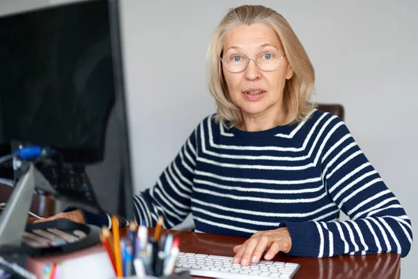 Volwassen middelbare leeftijd in glazen met behulp van laptop typen e-mail werken thuis kantoor, dame op zoek naar informatie op internet of communiceren online — Stockfoto