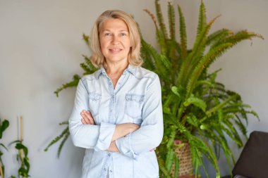 Güzel orta yaşlı sarışın kadın evde kameraya bakıyor.