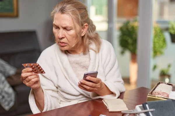 Sorunlu, olgun bir kadının portresi. Evde oturuyor, elinde telefon ve tabletlerle. — Stok fotoğraf