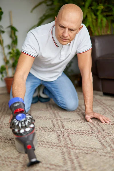 Guy met behulp van stofzuiger reinigen tapijt verwijdert stof schoon te houden in de woonkamer. — Stockfoto