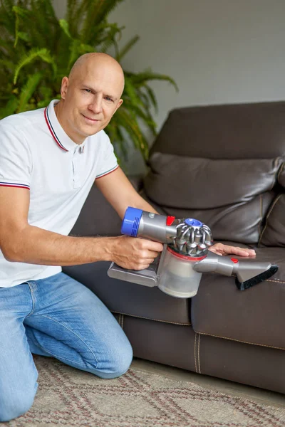 Man schoonmaken bank met handheld vacuüm tijdens het werken in de woonkamer. Schoonmaakdiensten. — Stockfoto