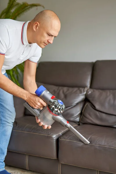 Homem sofá de limpeza com vácuo portátil enquanto trabalhava na sala de estar. Serviço de limpeza . — Fotografia de Stock