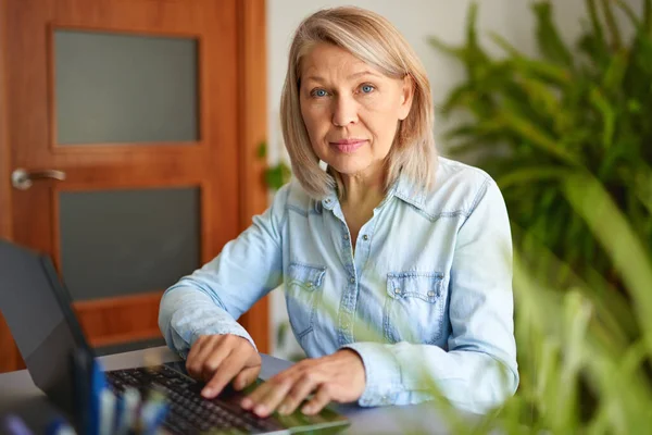 Ώριμη γυναίκα που κοιτάζει το φορητό υπολογιστή στο σπίτι. — Φωτογραφία Αρχείου