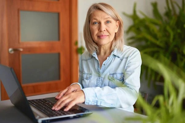 Ώριμη γυναίκα που κοιτάζει το φορητό υπολογιστή στο σπίτι. — Φωτογραφία Αρχείου