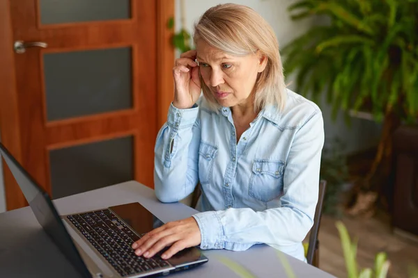 Volwassen vrouw op zoek naar laptop thuis. — Stockfoto