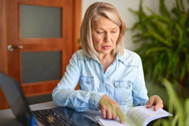 Evde dizüstü bilgisayara bakan olgun bir kadın..