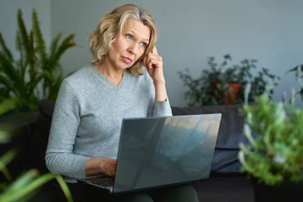 Mulher deitada em um sofá em casa concentrando-se como ela trabalha em um laptop . — Fotografia de Stock