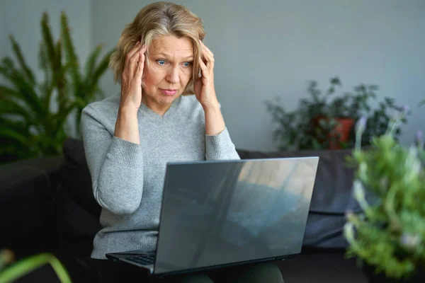 Mujer acostada en un sofá en casa concentrándose mientras trabaja en un portátil . — Foto de Stock