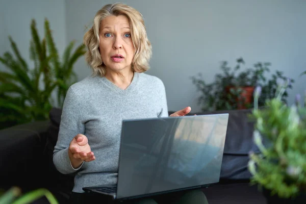 Здивована жінка сидить на дивані з ноутбуком вдома — стокове фото