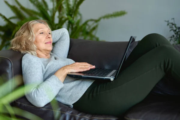 Mulher deitada em um sofá em casa com um laptop — Fotografia de Stock