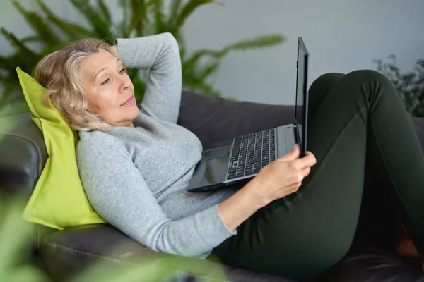 Mujer acostada en un sofá en casa con un portátil — Foto de Stock