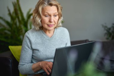 Evdeki kanepede uzanmış dizüstü bilgisayarla uğraşan bir kadın..