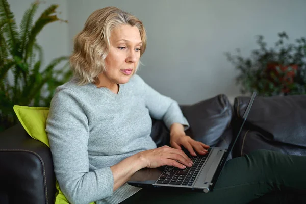 Жінка лежить на дивані вдома концентрується, коли вона працює на ноутбуці . — стокове фото