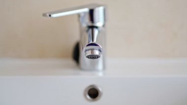 Adam musluğu açıyor ve lavaboyu suyla dolduruyor. Krom musluktan su akıyor. Banyo tesisatı..