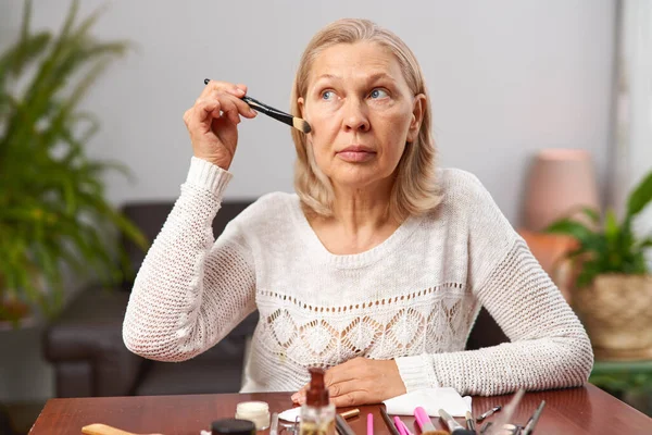 Krásná starší žena po použití make-up drží štětec. — Stock fotografie