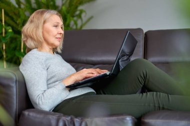 Evdeki kanepede uzanmış dizüstü bilgisayarla uğraşan bir kadın..