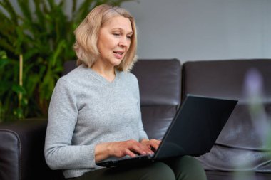 Evdeki kanepede oturan bir kadın dizüstü bilgisayarla çalışırken konsantre oluyor..