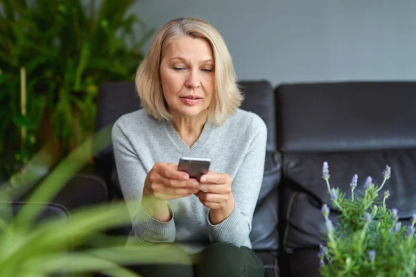 Serieuze vrouw woont een telefoongesprek zitten op een bank in de woonkamer thuis. — Stockfoto