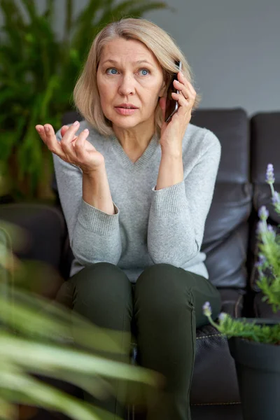 Femme sérieuse assistant à un appel téléphonique assis sur un canapé dans le salon à la maison . — Photo