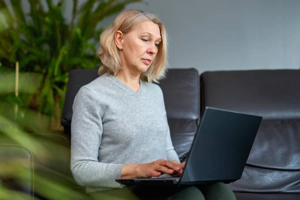 Mulher em um sofá em casa concentrando-se como ela trabalha em um laptop . — Fotografia de Stock