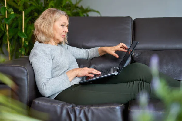 Mulher deitada em um sofá em casa concentrando-se como ela trabalha em um laptop . — Fotografia de Stock