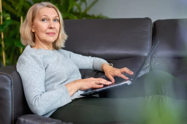 Mulher deitada em um sofá em casa concentrando-se como ela trabalha em um laptop . — Fotografia de Stock