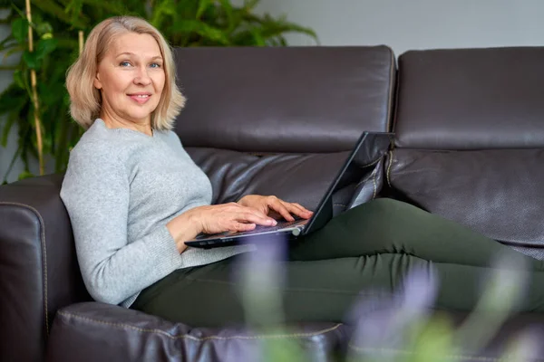 Woman lying on a sofa at home concentrating as she works on a laptop. — Stock Photo, Image