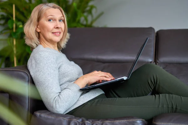 집에 있는 소파에 누워 있는 한 여자는 노트북으로 일하면서 집중 한다. — 스톡 사진