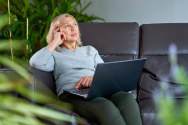 Evdeki kanepede oturan bir kadın dizüstü bilgisayarla çalışırken konsantre oluyor..