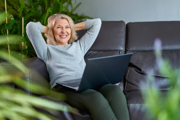 Mulher feliz em um sofá em casa concentrando-se como ela trabalha em um laptop . — Fotografia de Stock
