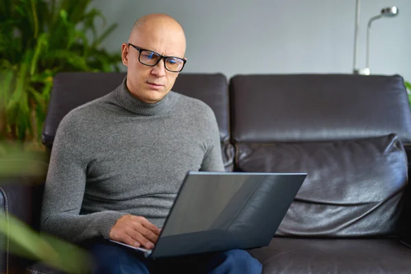 自宅で快適なソファの上の空白のノートパソコンで作業する男. — ストック写真