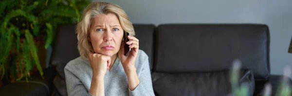 Mooie volwassen blonde vrouw praten op mobiele telefoon op de bank. — Stockfoto