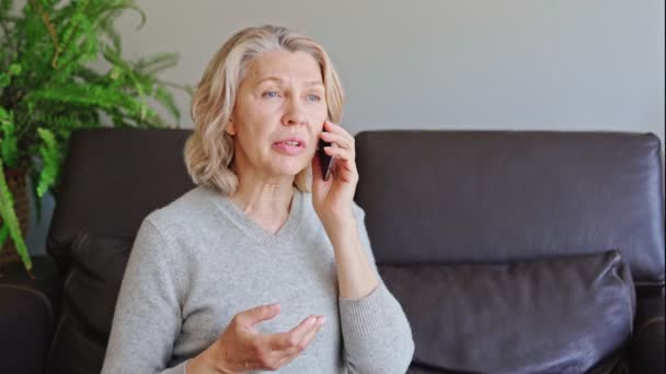 Volwassen vrouw met behulp van mobiele telefoon terwijl zitten op de bank thuis. — Stockvideo