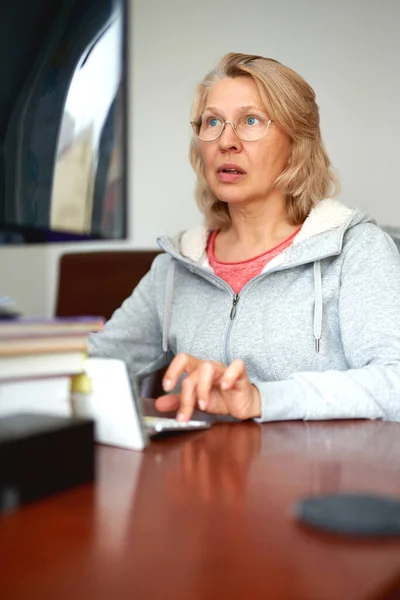 Mulher de meia-idade em óculos usando laptop digitando e-mail trabalhando em casa escritório, senhora procurando informações na internet ou se comunicando on-line — Fotografia de Stock