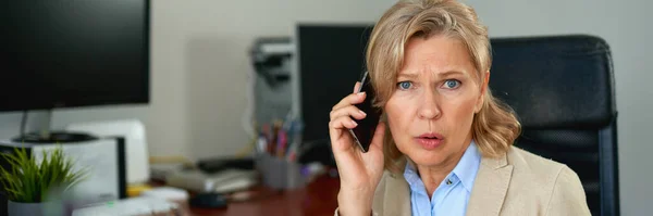 Senior businesswoman working and talking on smartphone at office interior. — Stock Photo, Image