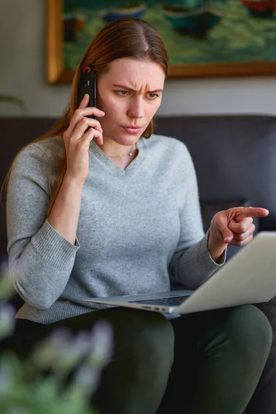 Gelukkig vrouw zitten op de bank met laptop en praten over de telefoon thuis. — Stockfoto