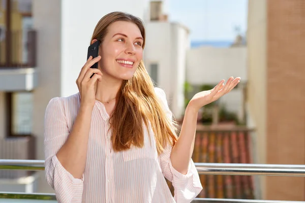 Portrait of a smiling casual woman holding smartphone on the balcony. — Stock Photo, Image